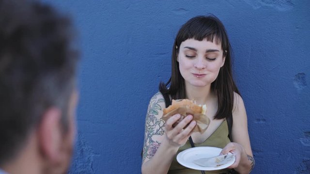 Cute hipster couple enjoys a quiet romantic dinner on outside terrace in restaurant, they share a delicious artisan made burger.
