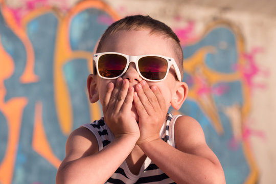 beautiful little boy wearing white sunglasses closed his mouth with hands