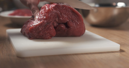 young female hand cutting raw beef with a knife on plastic board, 4k photo