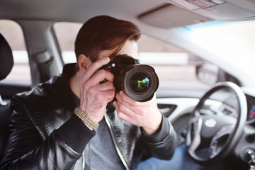 The man in the car reviews the photos on the camera. Spy, paparazzi, journalist, photographer.