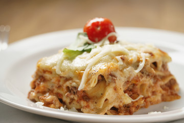 homemade lasagna portion on white plate on wood table, shallow focus