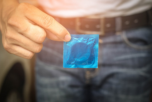 Man in white shirt holding condom in hand