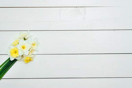Bright yellow daffodils in vase on white wooden table with copy space. Yellow and white narcissus. Greeting card. Top view