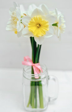 Bright yellow daffodils in vase on white wooden table, focus on one flower. Yellow and white narcissus. Greeting card