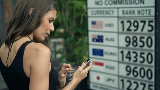 Woman with smartphone checking foreign currency in Indonesia
