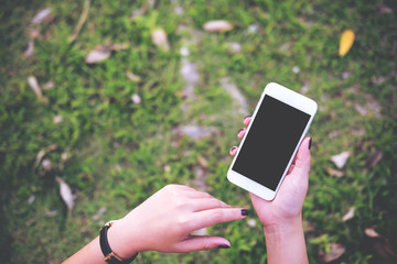 Mockup image of a hand holding white mobile phone with blank black screen in green garden floor background
