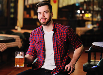 Bearded handsome man in a plaid shirt with a glass of beer