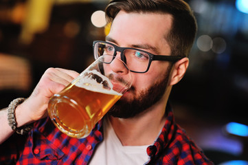 Bearded handsome man in a plaid shirt with a glass of beer