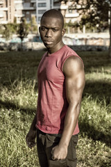 Naklejka na ściany i meble Portrait of a sexy young black man in urban park, wearing red sleeveless shirt