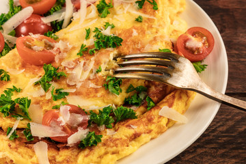 Closeup of omelette with parsley, cherry tomatoes, and fork