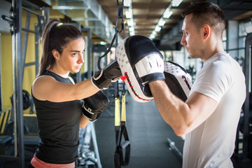 Young sporty woman punching her male partner with red boxing gloves at gym.