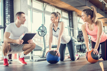Gym instructor assisting two sporty women with pilates balls in fitness center.