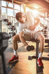 Young handsome man lifting weights in gym.