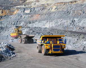 Excavator loading iron ore into heavy dump trucks on the opencast mining site