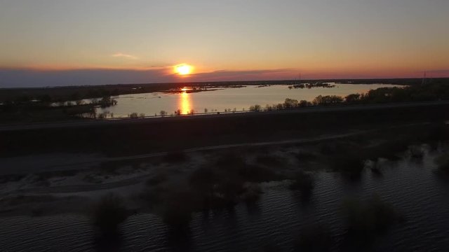 Aerial 4k of bridge near waters of river overflowing banks sunset. Copter fly along empty road dam or dike at flooded area in Belarus spring season top view with electricity poles and trees in water