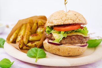 Big sandwich - hamburger with juicy beef burger, cheese, tomato, and red onion on light background and French fries.