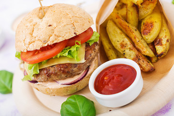 Big sandwich - hamburger with juicy beef burger, cheese, tomato, and red onion on light background and French fries.