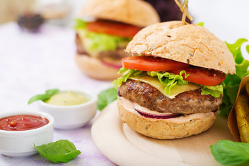 Big sandwich - hamburger with juicy beef burger, cheese, tomato, and red onion on light background and French fries.