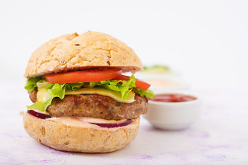 Big sandwich - hamburger with juicy beef burger, cheese, tomato, and red onion on light background and French fries.