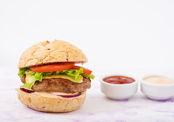 Big sandwich - hamburger with juicy beef burger, cheese, tomato, and red onion on light background and French fries.