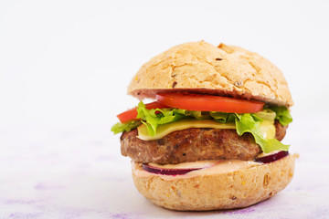 Big sandwich - hamburger with juicy beef burger, cheese, tomato, and red onion on light background and French fries.