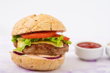 Big sandwich - hamburger with juicy beef burger, cheese, tomato, and red onion on light background and French fries.