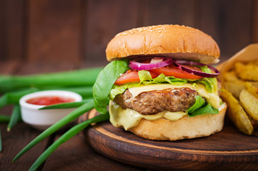 Big sandwich - hamburger with juicy beef burger, cheese, tomato,  and red onion on wooden background