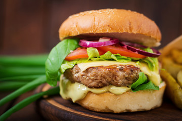 Big sandwich - hamburger with juicy beef burger, cheese, tomato,  and red onion on wooden background