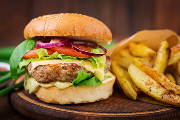 Big sandwich - hamburger with juicy beef burger, cheese, tomato,  and red onion on wooden background
