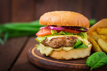Big sandwich - hamburger with juicy beef burger, cheese, tomato,  and red onion on wooden background