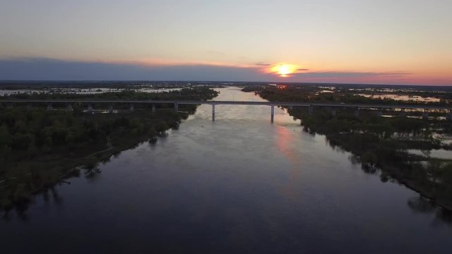 4k Fly above road bridge over wide river during high water spring season overflowed it banks with some cars moving aerial top view at sunset or sunrise time. Cargo logistics and transportation concept