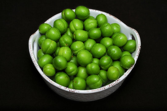 Heart form white bowl  full of Fresh green Plums Greengages on wooden Table. Georgian Fruit Alucha