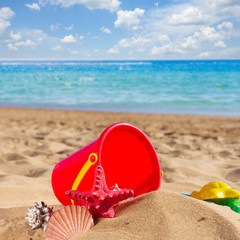 Fototapeta na wymiar bucket with seashells in sand on sea shore at sunny summer day