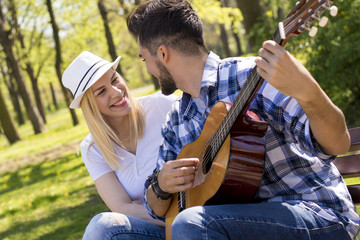 Couple sitting on bench and playing guitar on beautiful sunny day