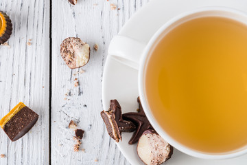 Cup of tea with raw handmade chocolate candies on white wooden background. Healthy breakfast with vegan sweets. Top view