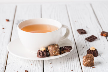 Cup of tea with raw handmade chocolate candies on white wooden background. Healthy breakfast with vegan sweets