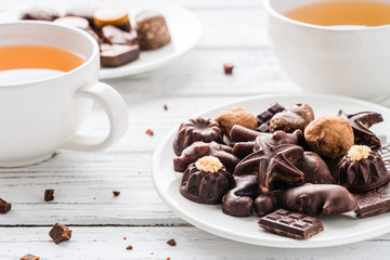 Raw handmade chocolate candies, two cups of tea on white wooden background. Healthy snack with vegan sweets