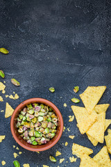 Chopped pistachios in a bowl with chips on dark background. Top view with copy space