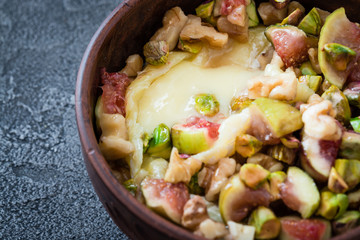 Baked soft cheese brie with figs, walnuts, pistachios and honey in a bowl. Snack concept. Selective focus. Dark background