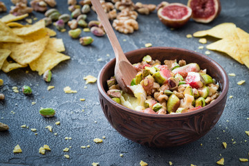 Baked soft cheese brie with figs, walnuts, pistachios and honey in a bowl with wooden spoon. Snack concept. Dark background