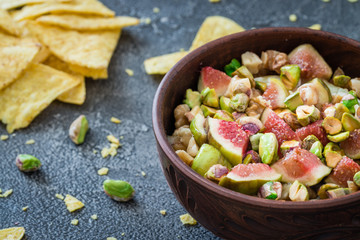 Raw chopped figs, walnuts, pistachios and honey with soft cheese in a bowl. Snack concept with chips. Selective focus. Dark background