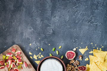 Ingredients layout for baking soft cheese brie with figs, walnuts, pistachios and honey. Snack concept with chips. Top view on dark background with copy space