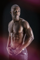 Fototapeta na wymiar Handsome shirtless muscular black young man, looking at camera, on dark background in studio shot
