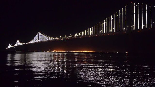 water view under the illuminated two levels of Oakland Bay Bridge, San Francisco
