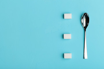 Spoon and sugar cubes on turquoise background, the view from the top with place for your text. Conceptual food photos