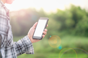man holding smartphone in hands against green spring background 
A Man using his Mobile phone outdoor, blank screen with lens flare effect.