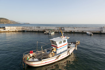 Fototapeta premium small fishing boat in harbor of agios nicolaos on greek peloponnese with sea and mountains in the background