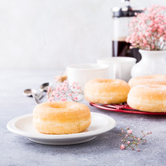 Doughnuts with powdered sugar and cups of coffee on light gray background. Selective focus. Copy space.
