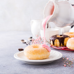 Doughnut with pink glaze poured from jug on light gray background. Selective focus. Copy space.