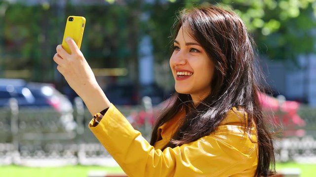 Selfie. Young beautiful woman communicates on cellphone sitting on bench in park